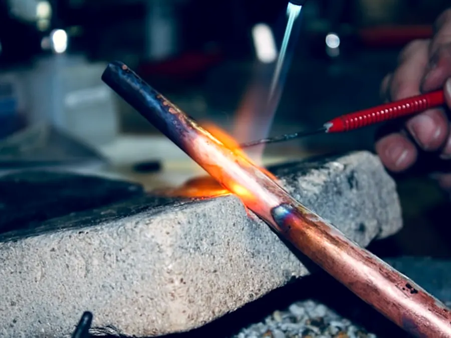 Copper pipe being soldered, torch flame on the joint.